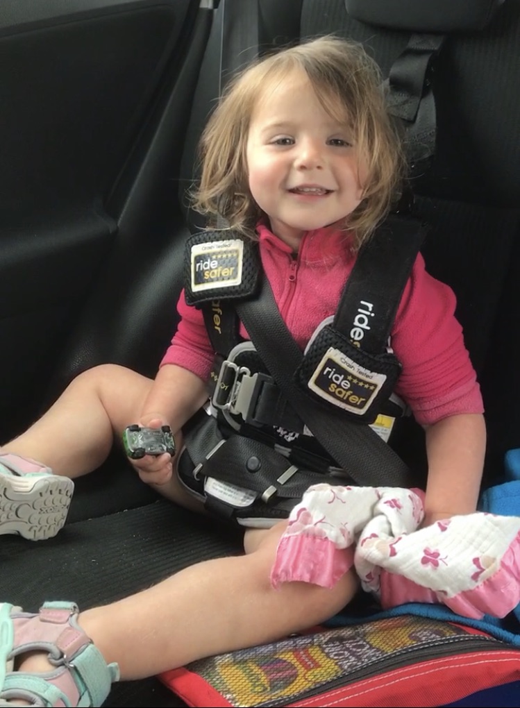 Toddler girl in pink sweatshirt using Ride Safer travel vest car seat alternative